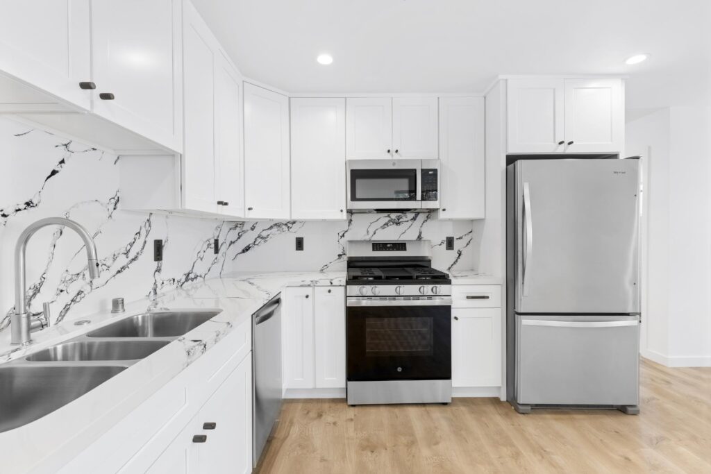 Modern ADU kitchen with white shaker cabinets, stainless steel appliances, marble quartz backsplash, and wood flooring — a renter-favorite upgrade by Los Angeles ADU builder M.E. Development Inc